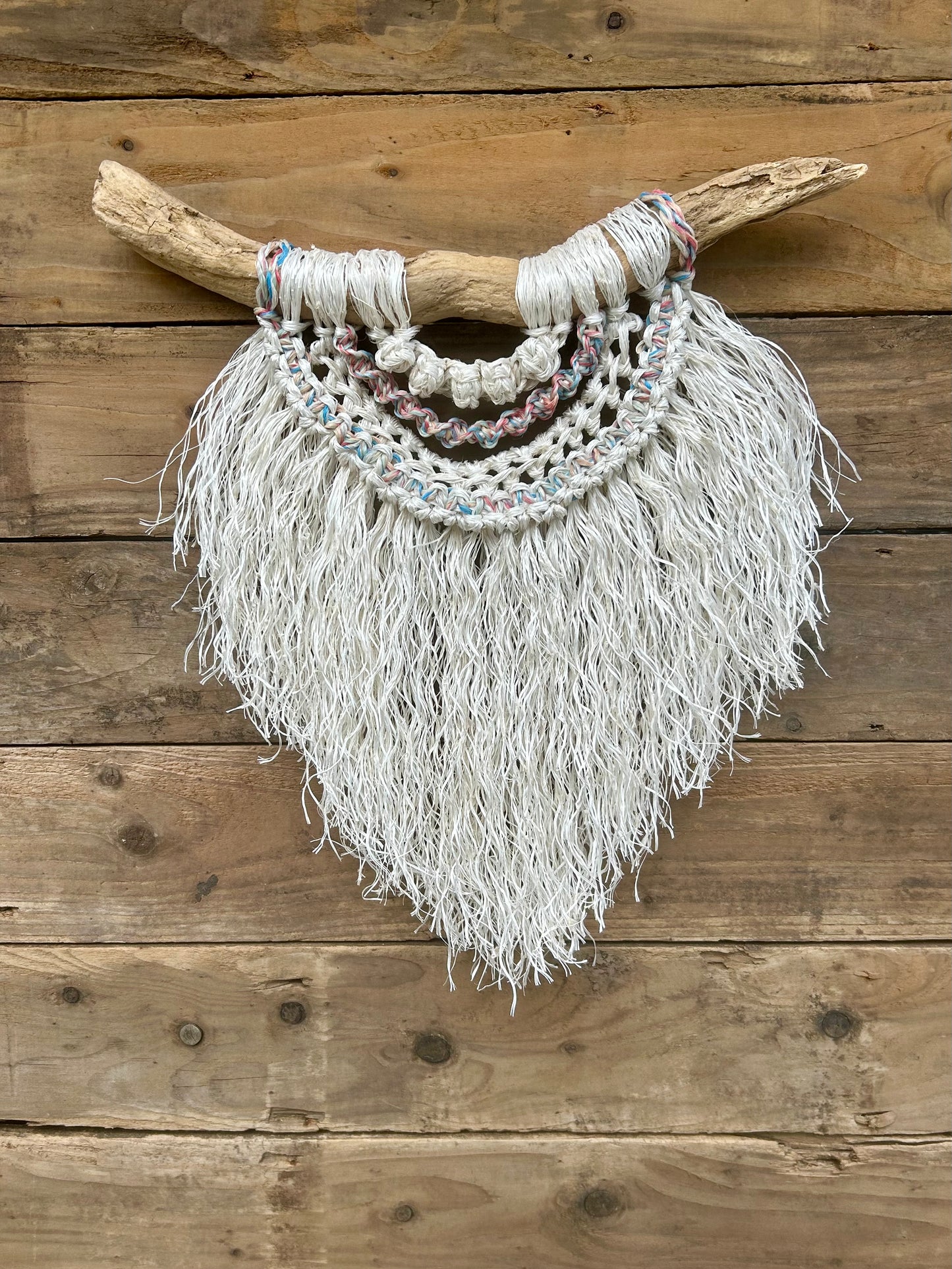 Sustainable rope wall art hand-knotted from repurposed rope with a soft white fringe and sun-bleached tones of red, white and blue, set on driftwood.