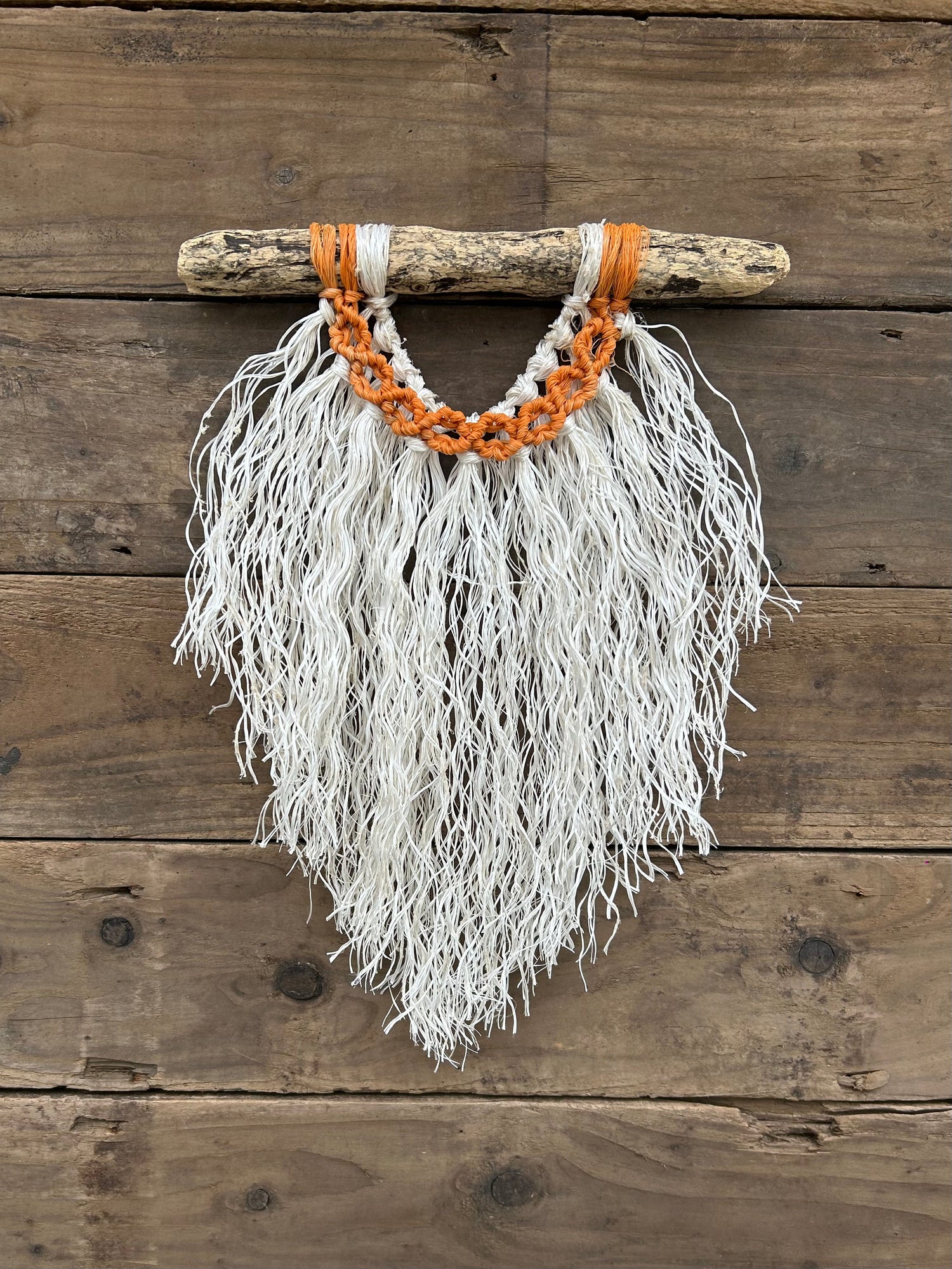 Handmade rope wall art made from salvaged fishing rope with sun-weathered orange circles and a soft white fringe, set on driftwood.