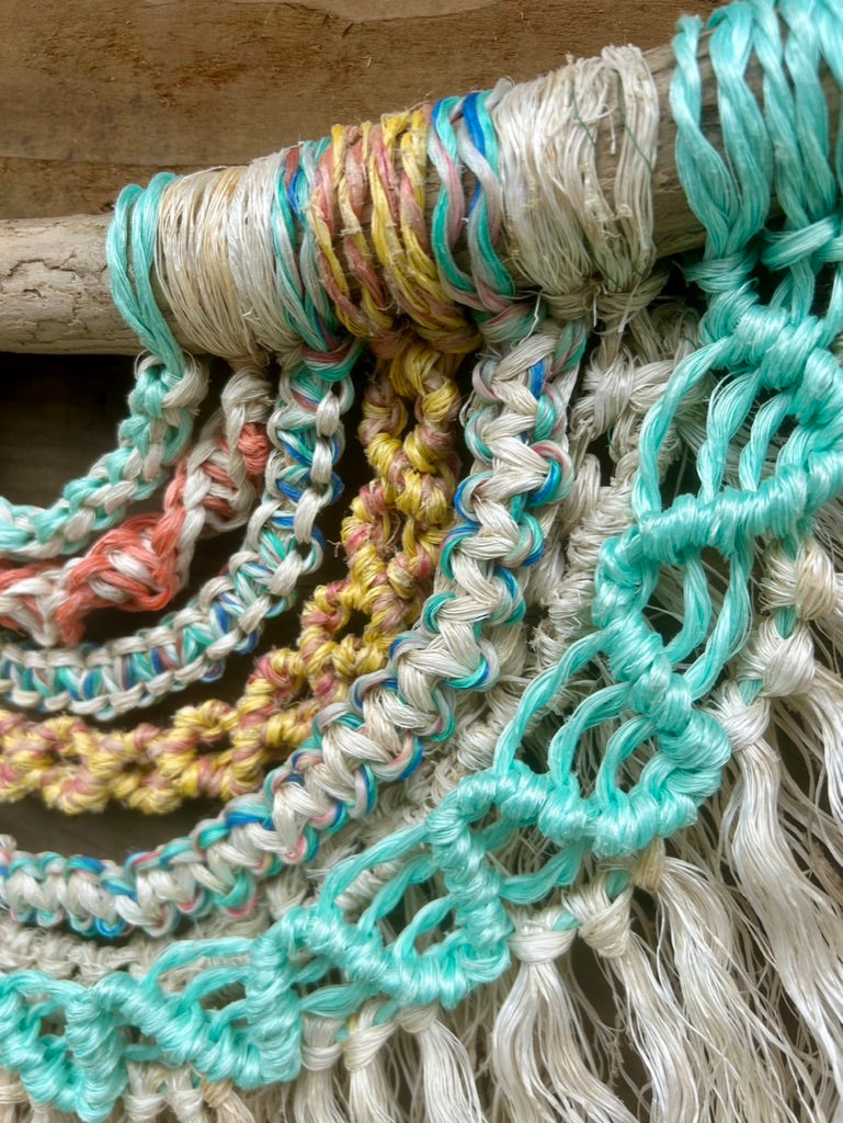 Detailed shot of rope wall art sustainably handmade from salvaged marine rope in soft, sun-bleached tones, set on driftwood.