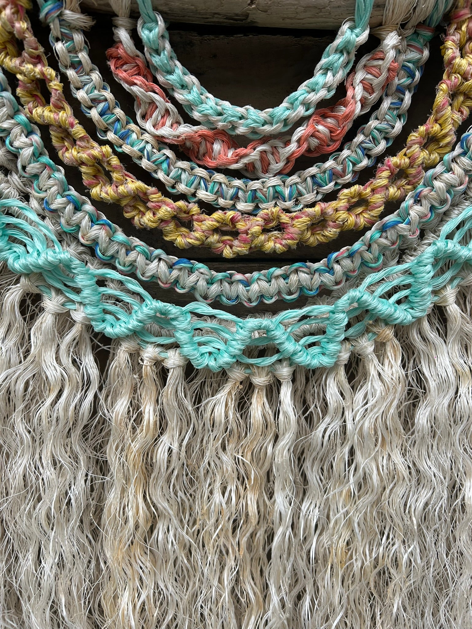Sustainable handmade coastal wall piece with layered knotting in sea-worn coastal tones and a weathered white textured fringe showing rust markings from its previous life.