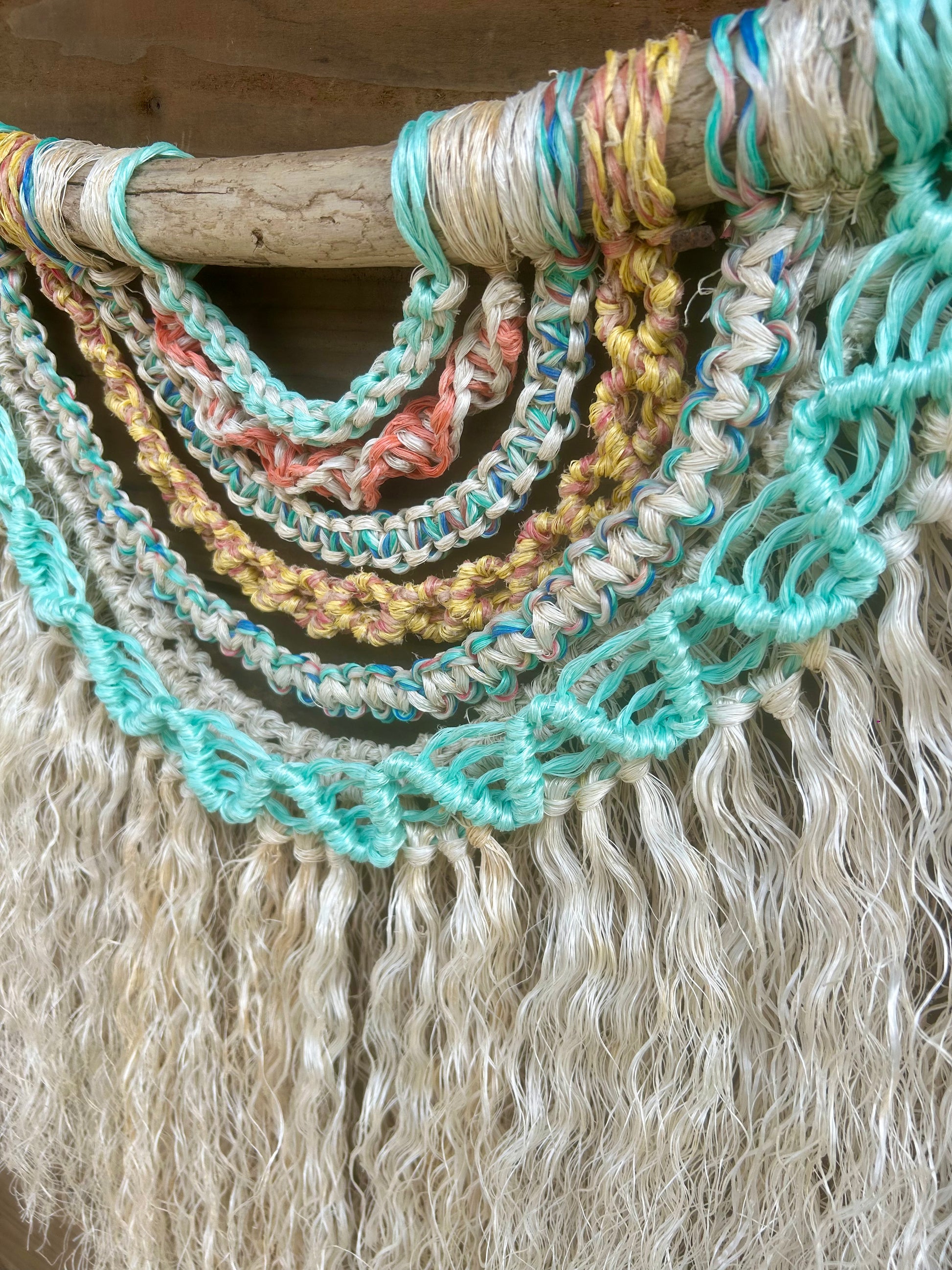 Close up shot of sustainable coastal wall art, showing knot patterns in soft, sun-washed colours, handcrafted by repurposing retired fishing ropes, set on driftwood.