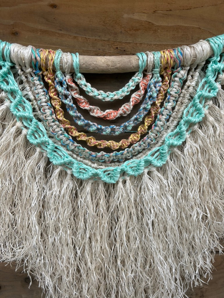 Handmade coastal wall art made from repurposed fishing ropes, with sun-bleached tones and a soft white textured fringe, set on driftwood.