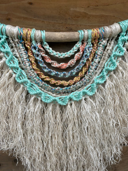 Handmade coastal wall art made from repurposed fishing ropes, with sun-bleached tones and a soft white textured fringe, set on driftwood.