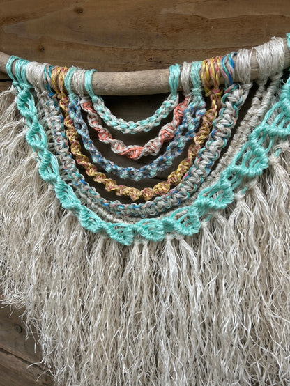 Handmade coastal wall piece using sun-bleached salvaged marine rope with layered knots and a textured weathered white fringe on driftwood.