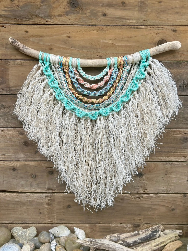 Statement coastal wall art sustainably handmade from salvaged marine ropes, in soft coastal tones with a textured white fringe set on driftwood.