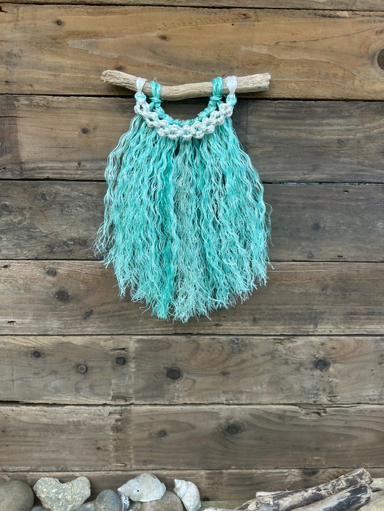 Repurposed fishing rope coastal wall hanging handcrafted from ocean waste with a sea-green fringe and weathered white band of flower knots.