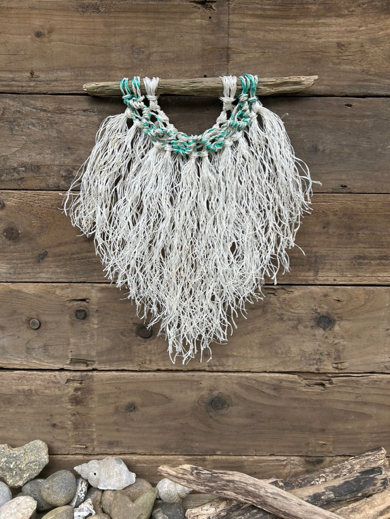 Weathered white coastal wall hanging hand-knotted from reclaimed fishing ropes featuring a sea-green and white wave on driftwood.