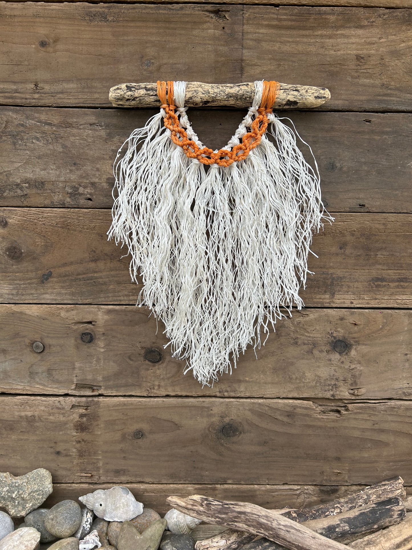 Coastal rope macramé wall hanging handmade using repurposed fishing ropes with weathered white fringe and sun-worn orange circles on driftwood.