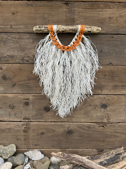 Coastal rope macramé wall hanging handmade using repurposed fishing ropes with weathered white fringe and sun-worn orange circles on driftwood.