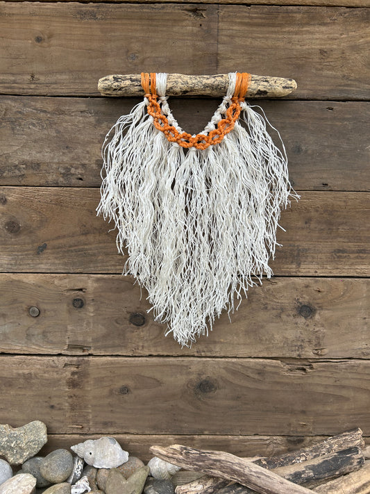 Coastal rope macramé wall hanging handmade using repurposed fishing ropes with weathered white fringe and sun-worn orange circles on driftwood.