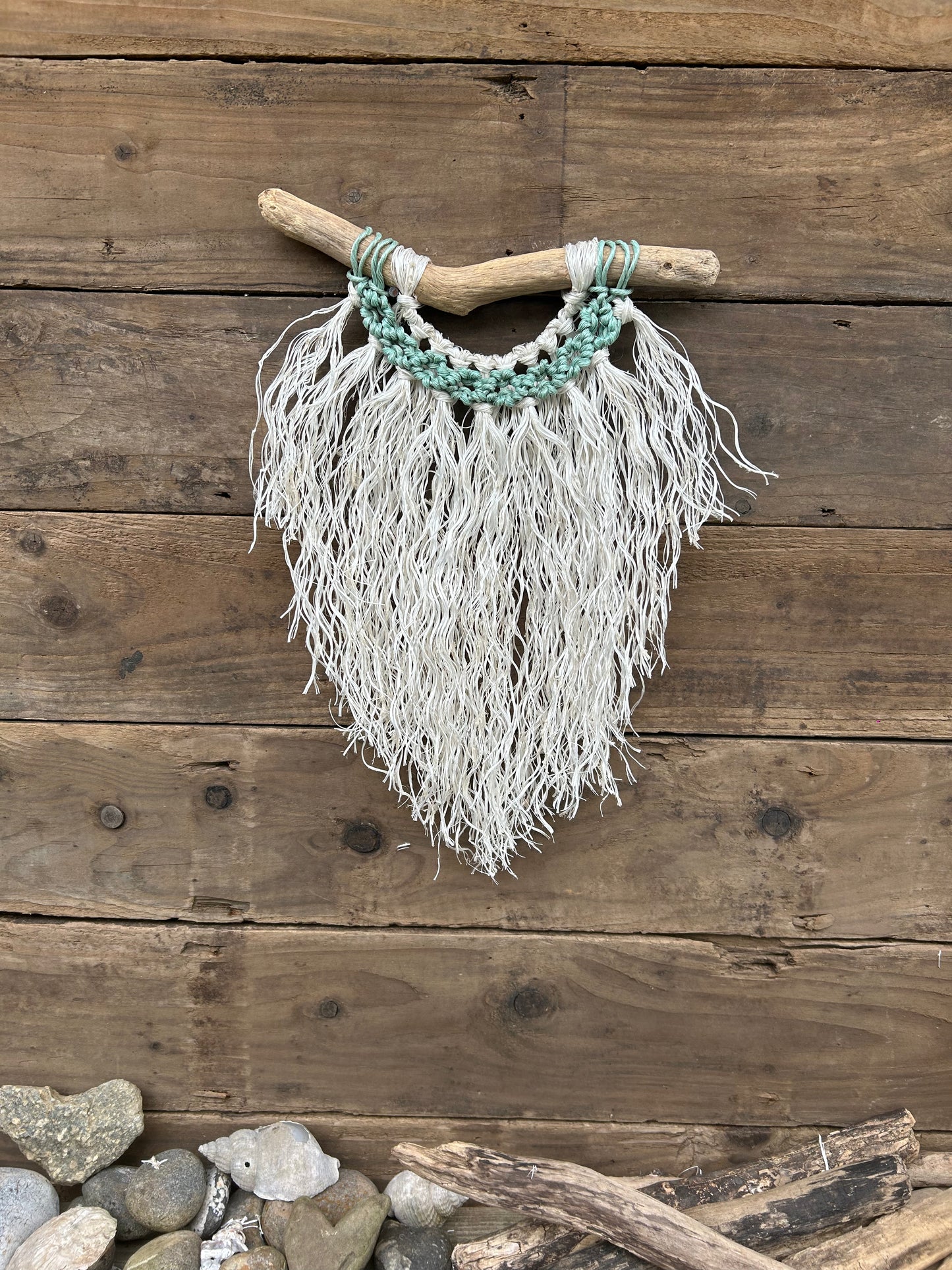 Coastal inspired wall hanging handcrafted by repurposing retired fishing ropes. Weathered white fringe with sea-foam circles on driftwood, perfect coastal décor.