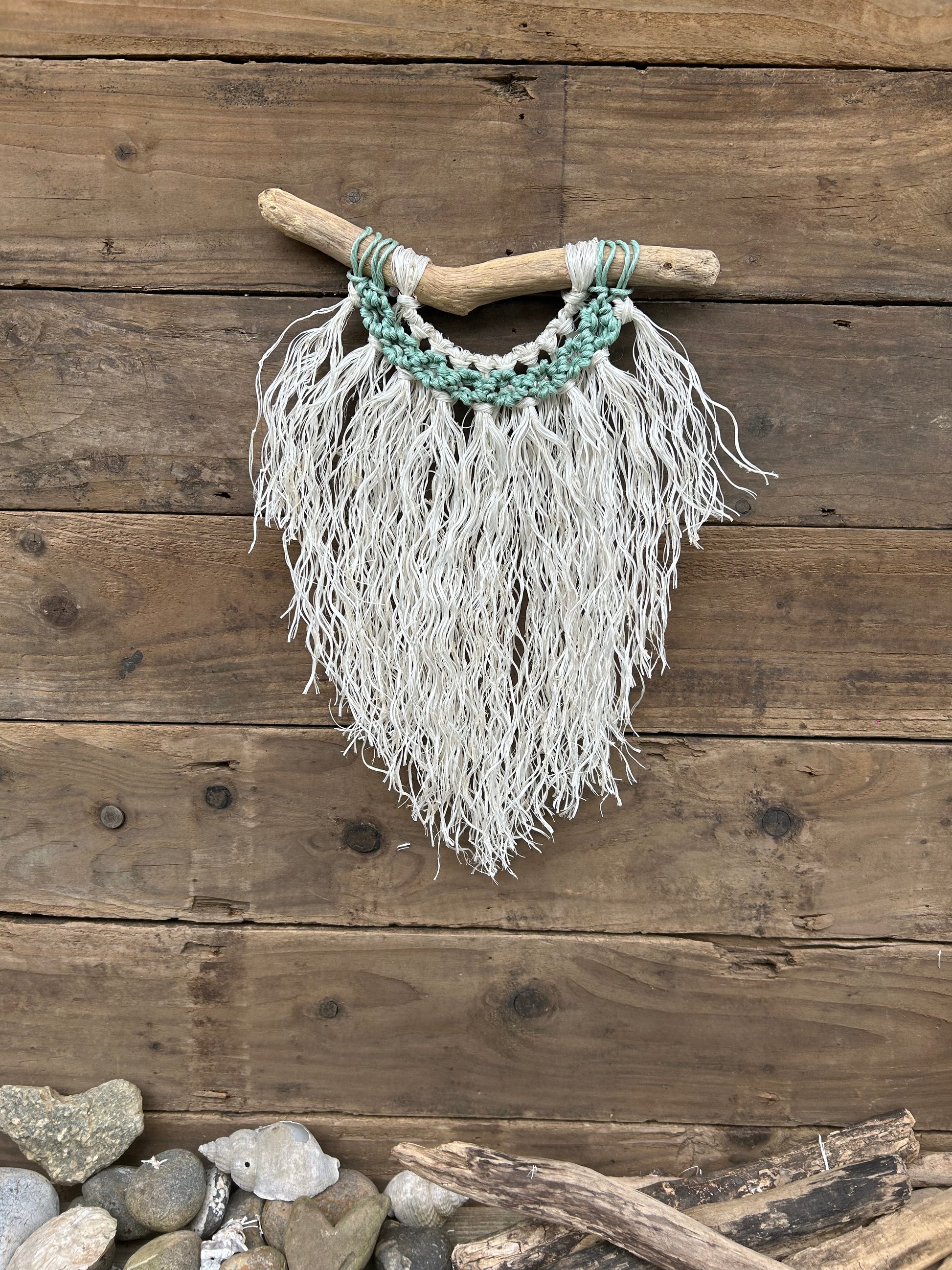 Coastal inspired wall hanging handcrafted by repurposing retired fishing ropes. Weathered white fringe with sea-foam circles on driftwood, perfect coastal décor.