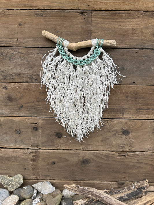 Coastal inspired wall hanging handcrafted by repurposing retired fishing ropes. Weathered white fringe with sea-foam circles on driftwood, perfect coastal décor.