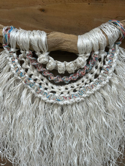 Sustainable coastal wall piece handcrafted from reclaimed fishing rope with a soft white fringe and sun-bleached tones of red, white and blue, set on driftwood.