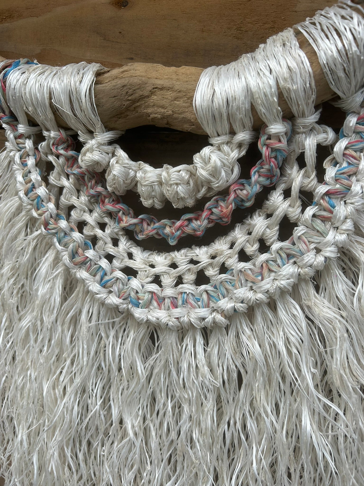 Handmade rope wall art crafted from repurposed fishing ropes, showing texture and sun-bleached tones of red, white and blue, set on driftwood.