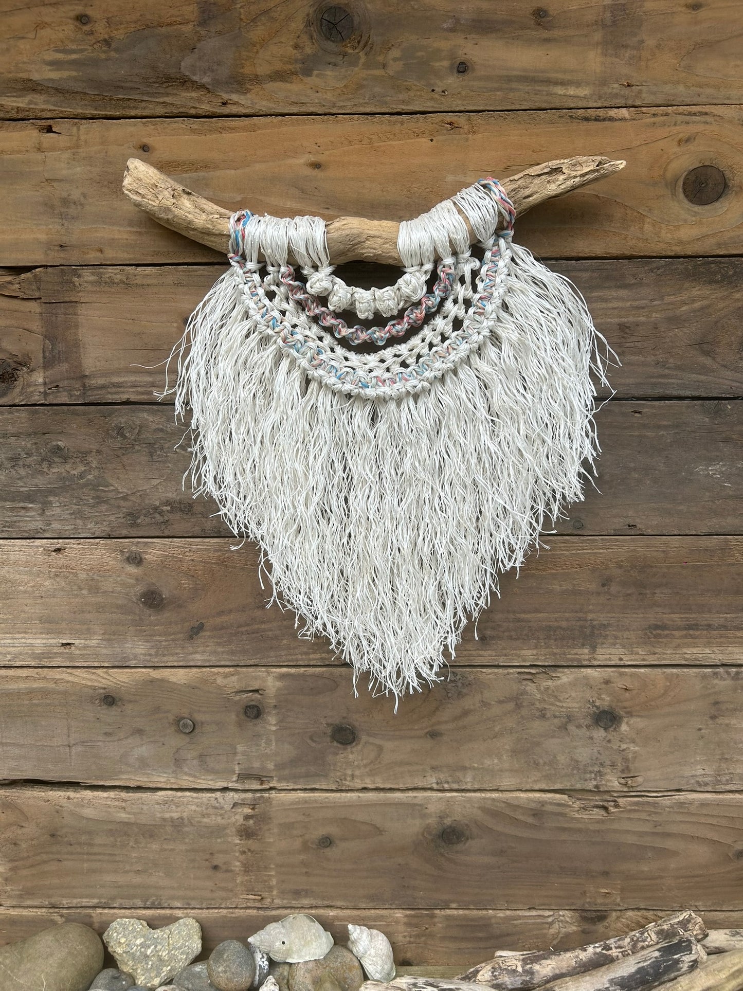 Sustainable coastal wall piece handcrafted from salvaged rope with soft, sun-bleached tones of red, white and blue, set on driftwood.