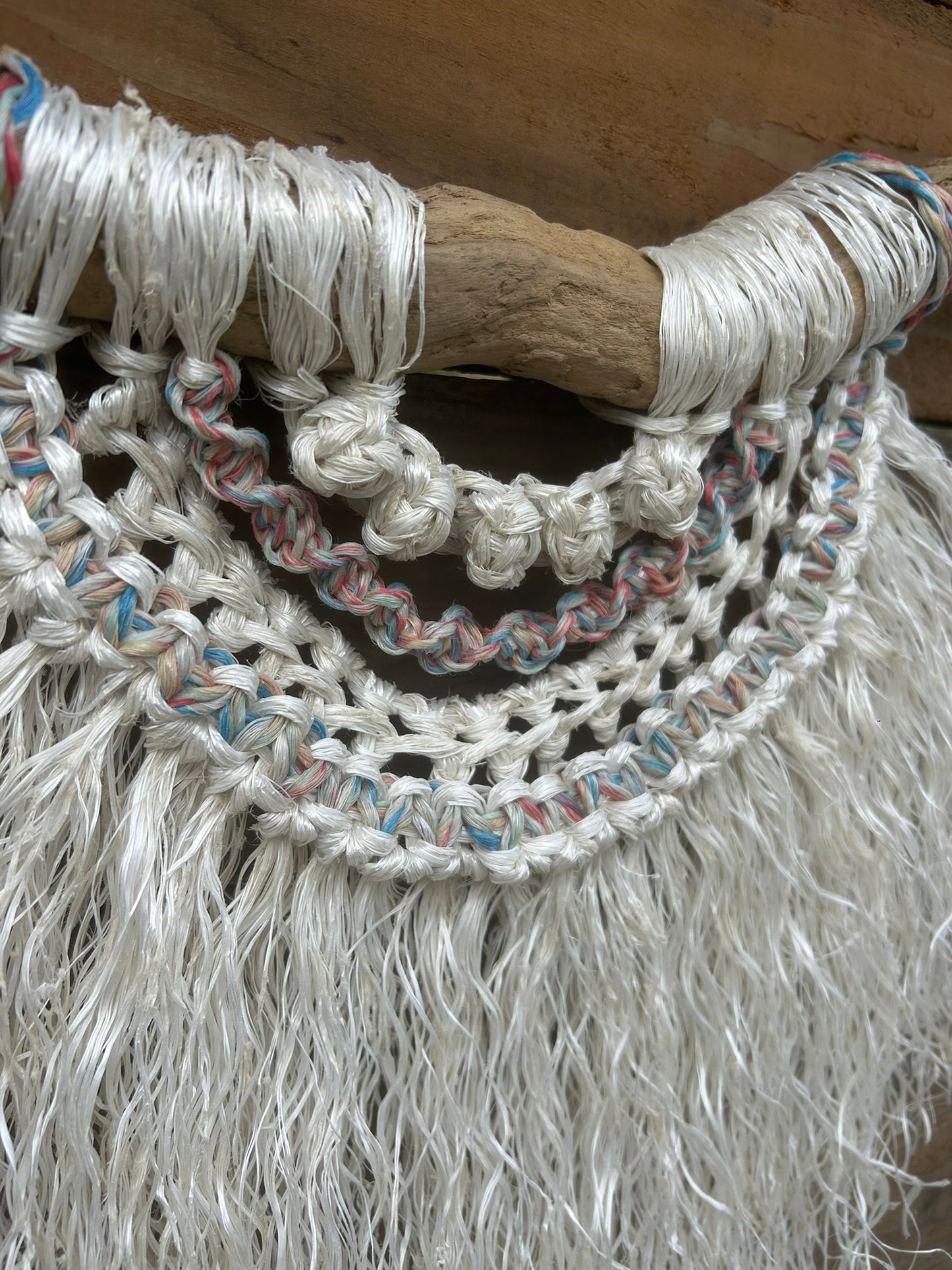 Side detail of hand-knotted rope wall art, crafted from salvaged fishing rope, highlighting texture and sun-faded tones of red, white and blue, set on driftwood.