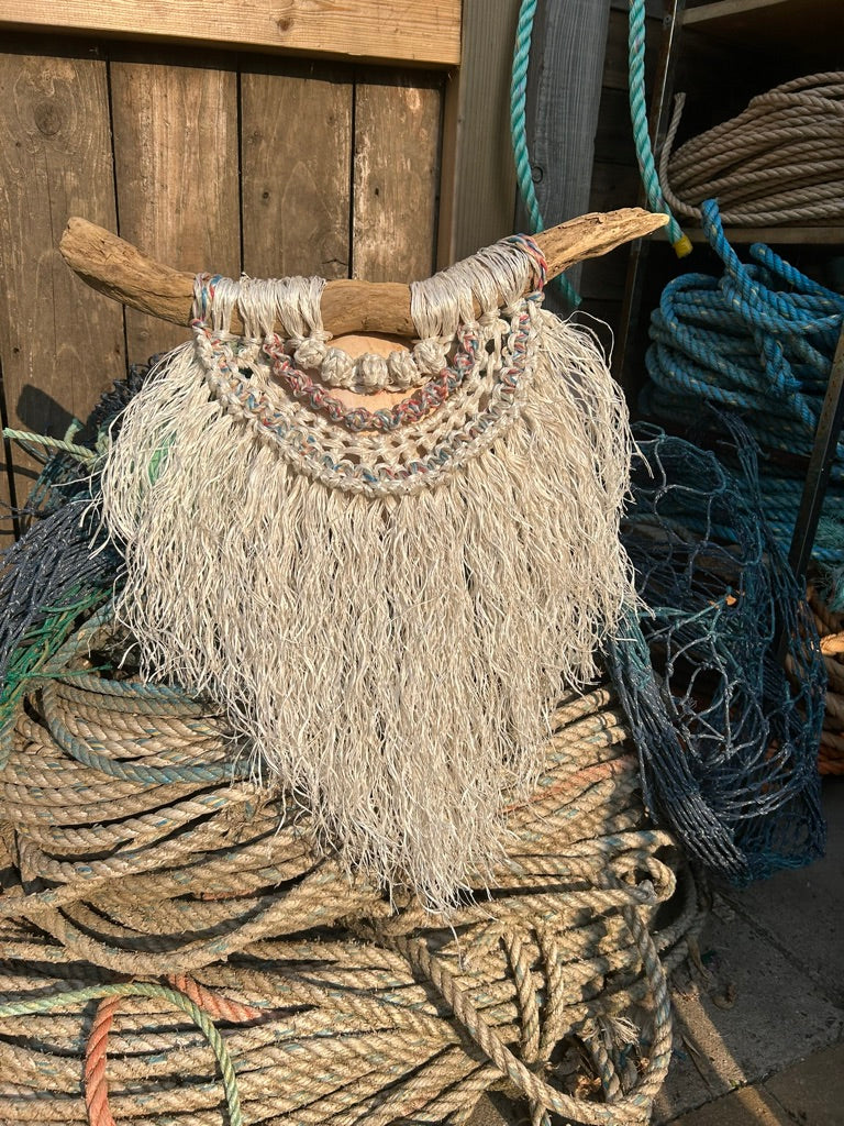 Handcrafted textured coastal rope wall art on driftwood, in sea-washed red, white and blue on a pile of retired fishing rope and netting.