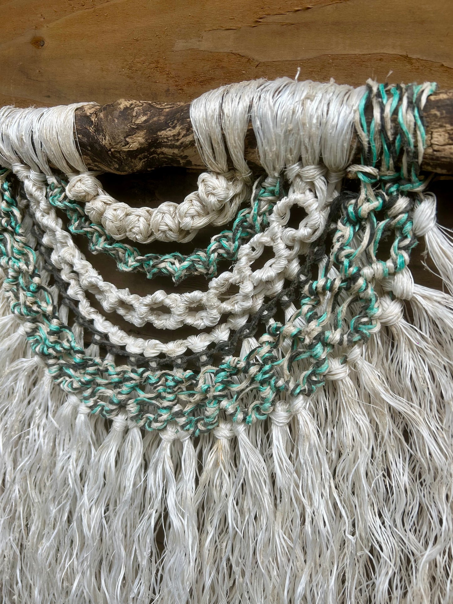 Textured coastal wall art handmade from reclaimed fishing ropes, with soft white fringe and rock pool tones of green and black, set on driftwood.