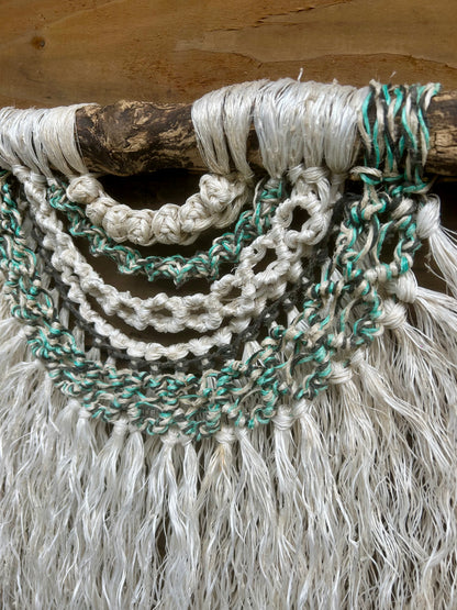 Textured coastal wall art handmade from reclaimed fishing ropes, with soft white fringe and rock pool tones of green and black, set on driftwood.