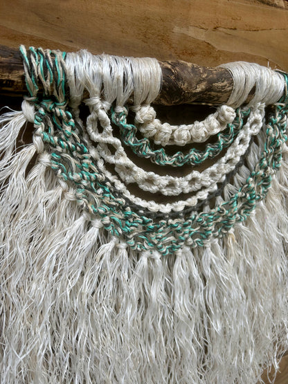 Sustainable, handcrafted macramé wall hanging, created from recycled fishing ropes in tidal tones of soft white, green and black, set on driftwood.