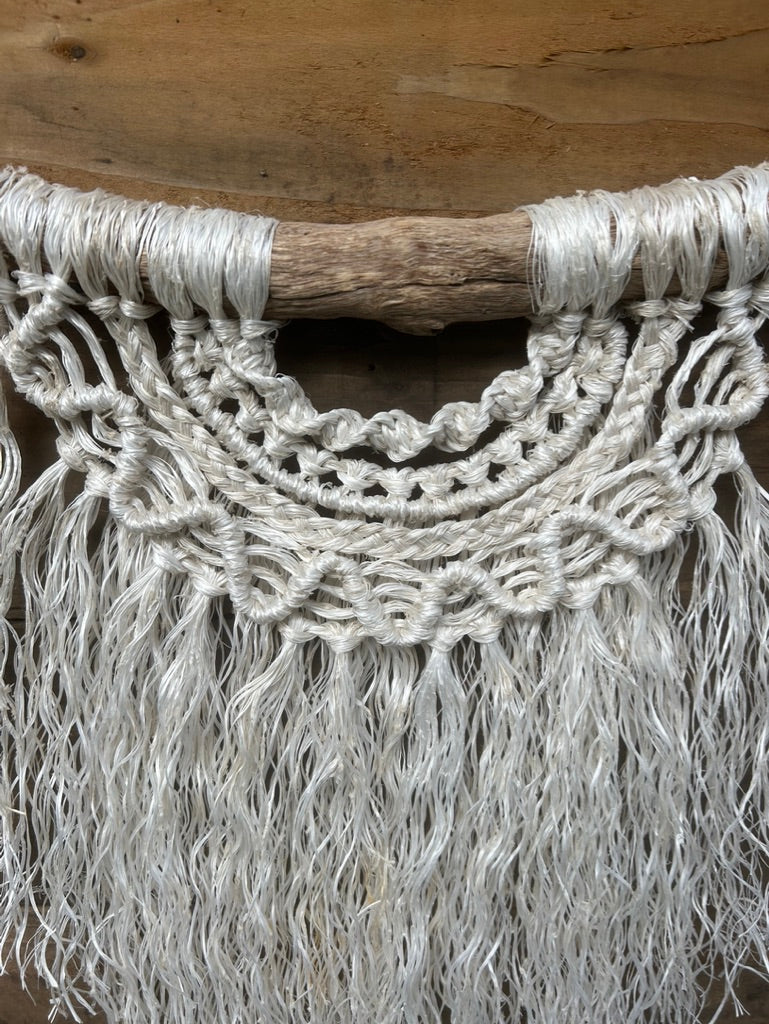 Coastal wall hanging handcrafted from salvaged rope showing texture and layered knotting in soft white, set on driftwood.