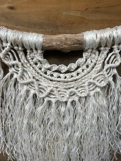 Coastal wall hanging handcrafted from salvaged rope showing texture and layered knotting in soft white, set on driftwood.