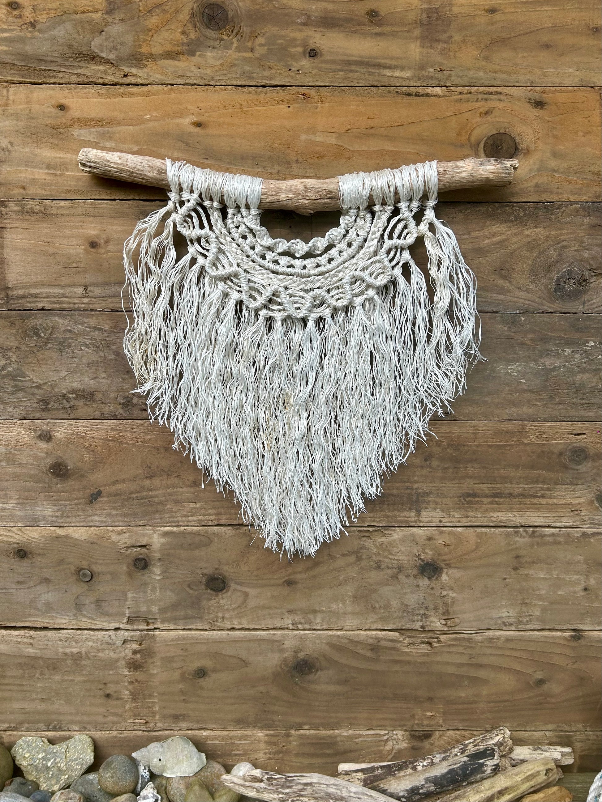 Boho coastal interior wall hanging, handmade from repurposed fishing rope, in soft, textured, weathered white, set on driftwood.