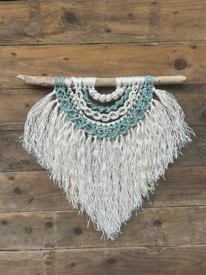 Eco-friendly wall art handmade from repurposed fishing ropes, in coastal tones of sea blues and greens with a soft white fringe, set on driftwood.