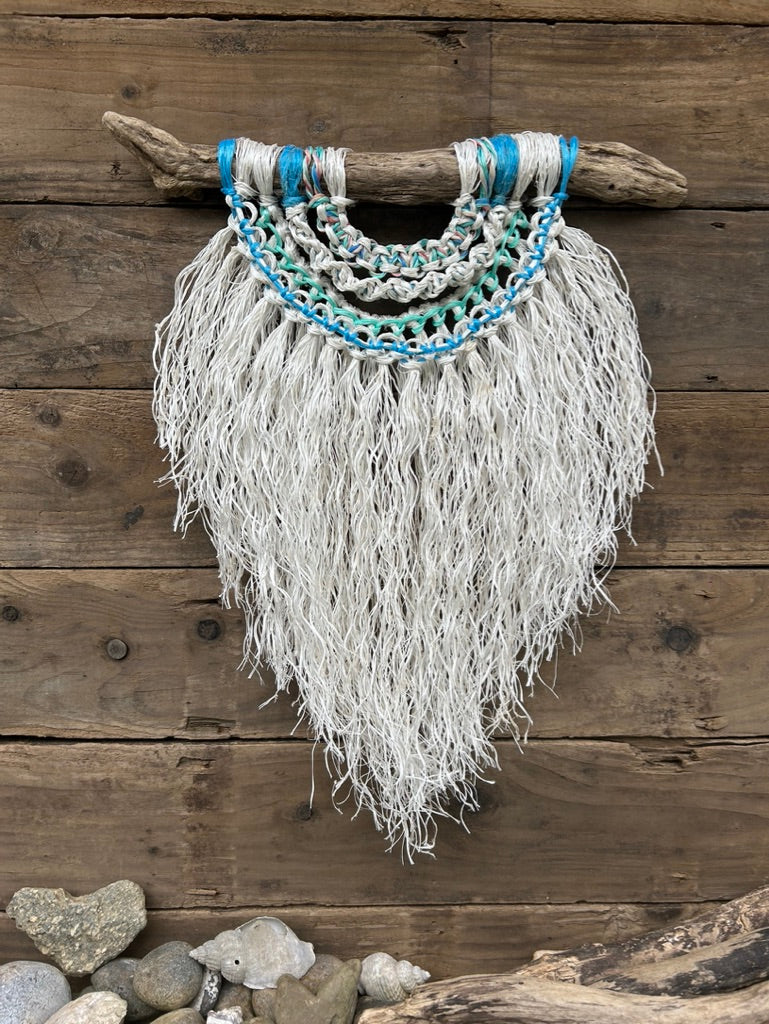 Coastal inspired eco-friendly wall art, handcrafted from retired fishing ropes with a textured, soft white fringe and sea blues and greens, set on driftwood.