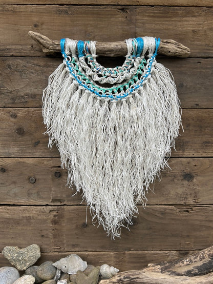 Coastal inspired eco-friendly wall art, handcrafted from retired fishing ropes with a textured, soft white fringe and sea blues and greens, set on driftwood.