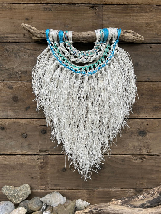 Coastal inspired eco-friendly wall art, handcrafted from retired fishing ropes with a textured, soft white fringe and sea blues and greens, set on driftwood.
