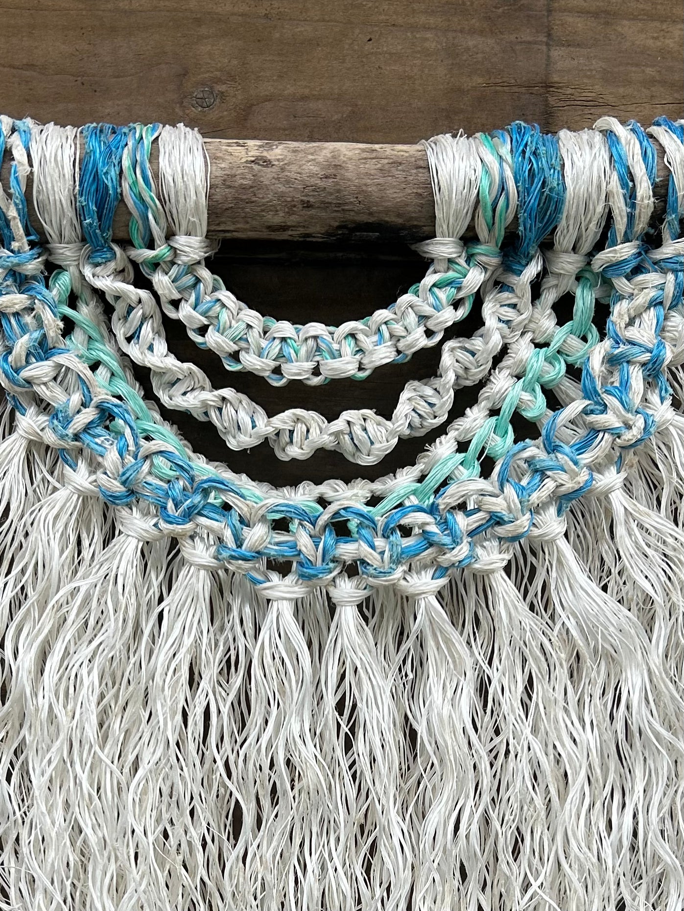 Close-up shot of handmade coastal inspired, eco-friendly wall art, in soft white and sea blues and greens, set on driftwood.