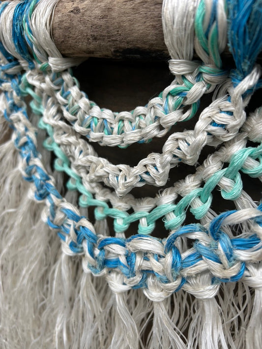 Close-up of sea green and blue knots on eco-friendly costal wall hanging, made from repurposed fishing ropes, set on driftwood.
