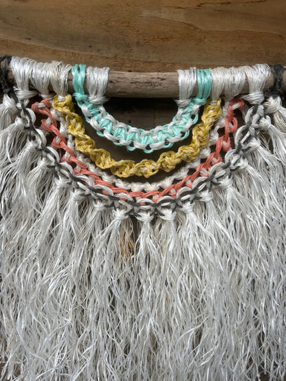 Close-up photo of reggae inspired ocean wall art, handcrafted from reclaimed fishing ropes, in weathered tones of white, green, yellow, red and black, set on driftwood.