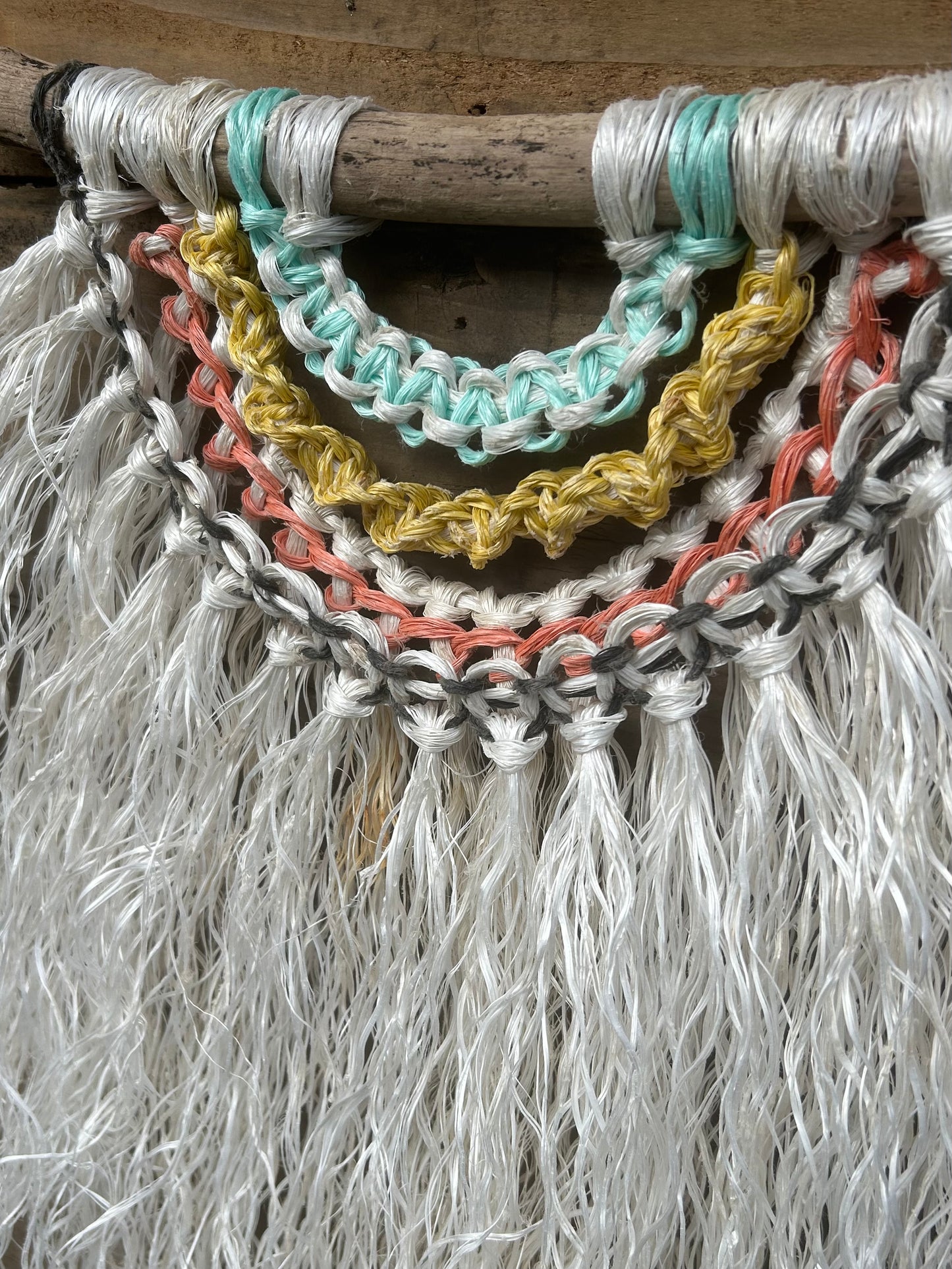 Detailed shot of reggae inspired coastal wall hanging, hand-knotted from ocean waste, set on driftwood.