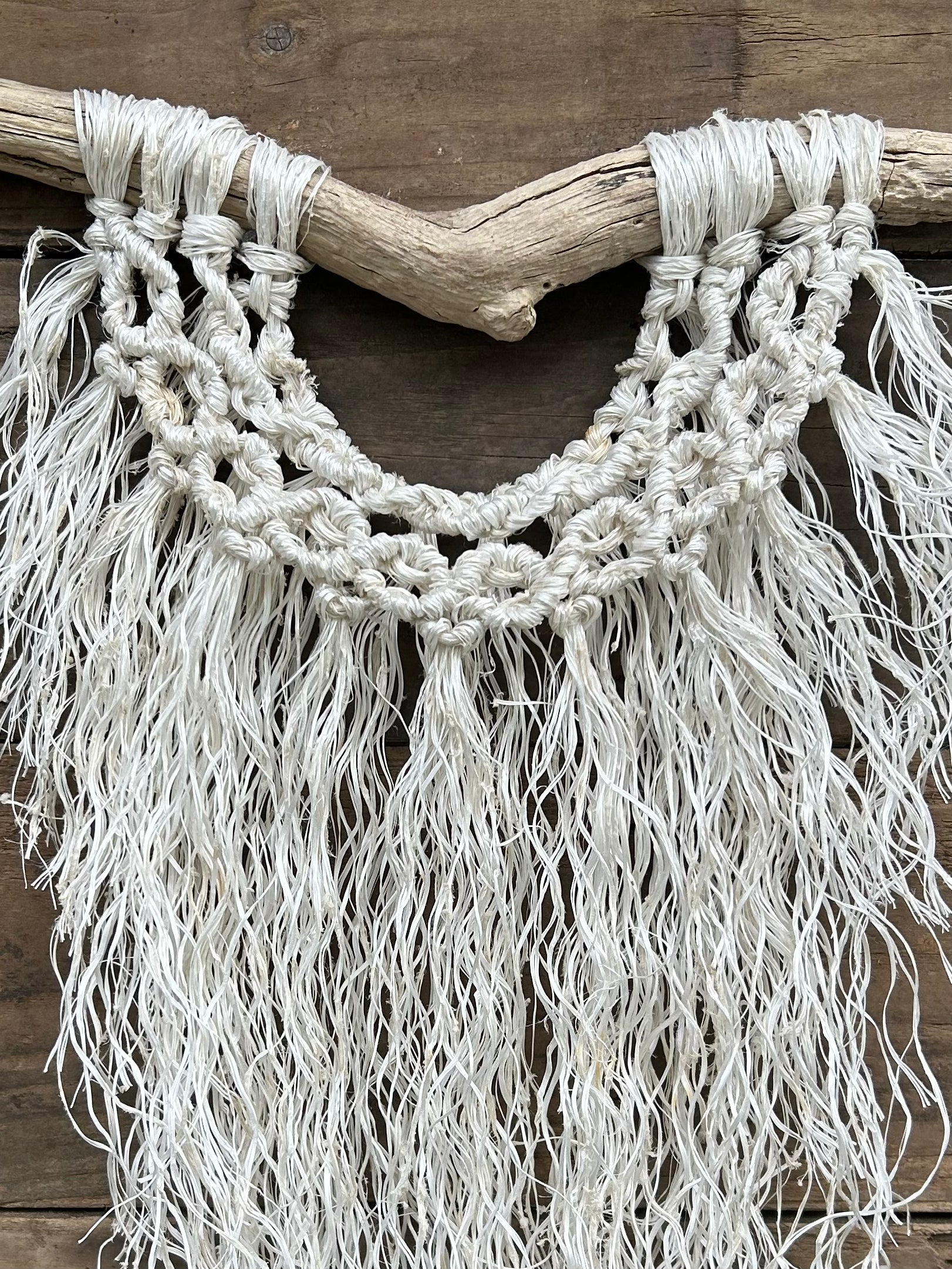 Close-up of textured, weathered white coastal decor wall hanging, created from repurposed retired fishing ropes, set on driftwood.