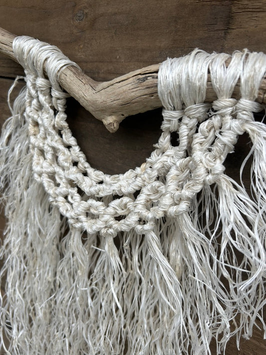Close-up photo showing textured layers of boho wall hanging, handcrafted from reclaimed fishing rope, with a soft white fringe and band of circle knots, set on driftwood.