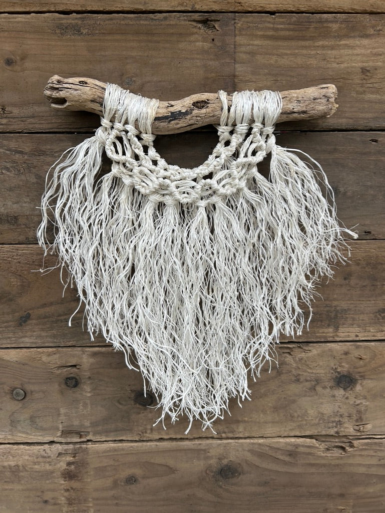 Layered boho coastal rope wall art, handmade sustainably from retired fishing rope, with a soft white fringe and a band of wave knots, set on driftwood.