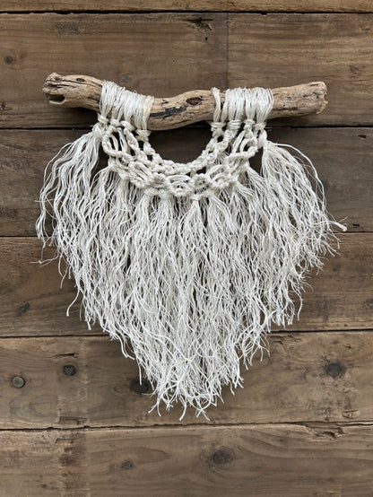 Layered boho coastal rope wall art, handmade sustainably from retired fishing rope, with a soft white fringe and a band of wave knots, set on driftwood.