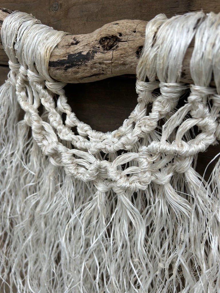 Close-up of wave knots on ocean inspired macrame wall hanging, handmade from reclaimed fishing ropes, in weathered white, set on driftwood.