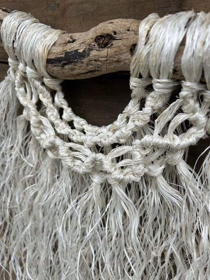 Close-up of wave knots on ocean inspired macrame wall hanging, handmade from reclaimed fishing ropes, in weathered white, set on driftwood.